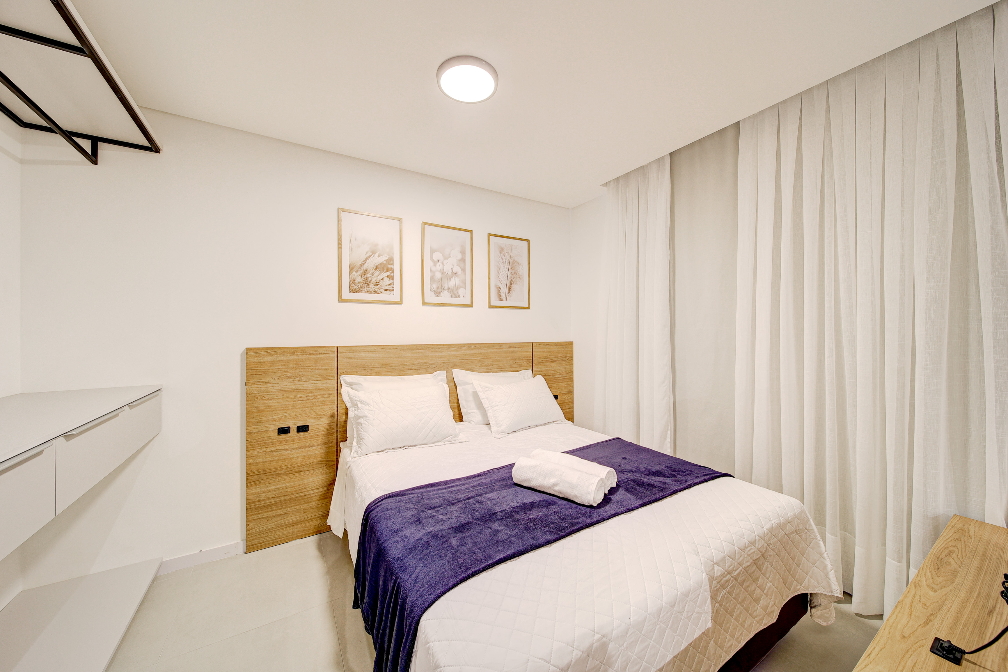 Dormitório acolhedor com cama de casal, cabeceira em madeira e sol da tarde
